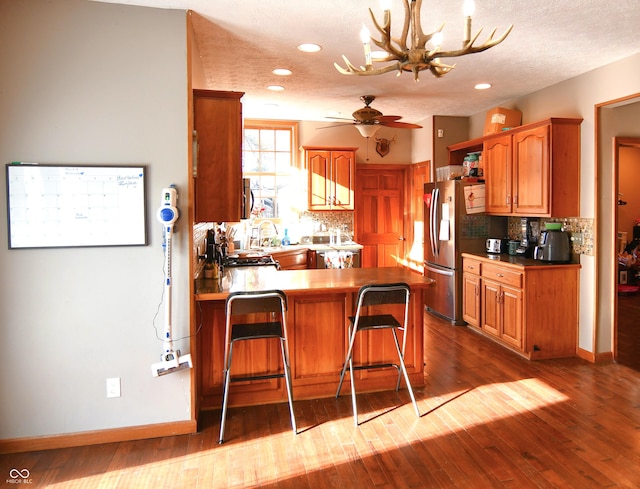 kitchen with a peninsula, freestanding refrigerator, backsplash, and dark wood finished floors