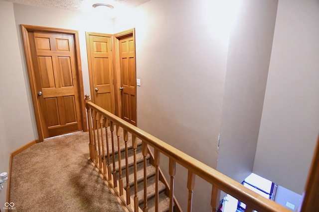 corridor with baseboards, carpet flooring, a textured ceiling, and an upstairs landing