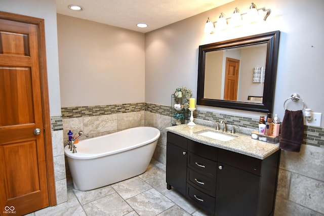 bathroom with tile walls, wainscoting, a freestanding bath, and vanity