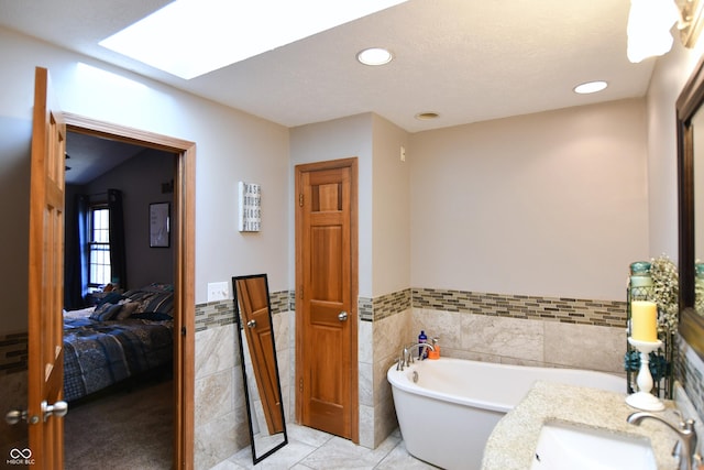 ensuite bathroom with a skylight, tile walls, a soaking tub, ensuite bath, and a sink