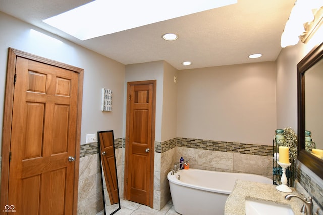 full bath with a skylight, a sink, a freestanding tub, tile walls, and recessed lighting