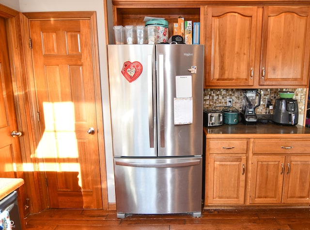 kitchen with dark wood-style floors, brown cabinets, stainless steel appliances, dark countertops, and backsplash