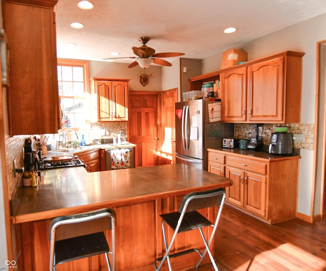 kitchen with stainless steel appliances, a peninsula, a sink, decorative backsplash, and dark wood-style floors