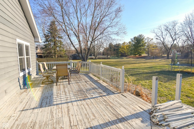 wooden terrace featuring a trampoline, outdoor dining area, and a lawn