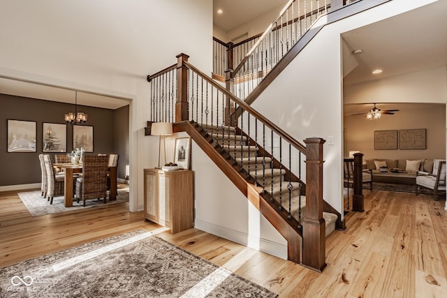 stairs with ceiling fan with notable chandelier, a high ceiling, baseboards, and wood-type flooring