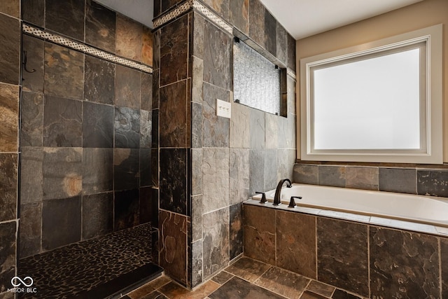 bathroom featuring a bath, a tile shower, and stone tile flooring