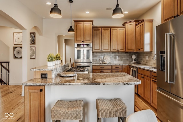 kitchen with a sink, a center island, light wood-style floors, appliances with stainless steel finishes, and brown cabinetry