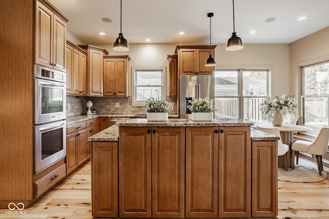 kitchen with brown cabinets, tasteful backsplash, a center island, light wood-style floors, and appliances with stainless steel finishes