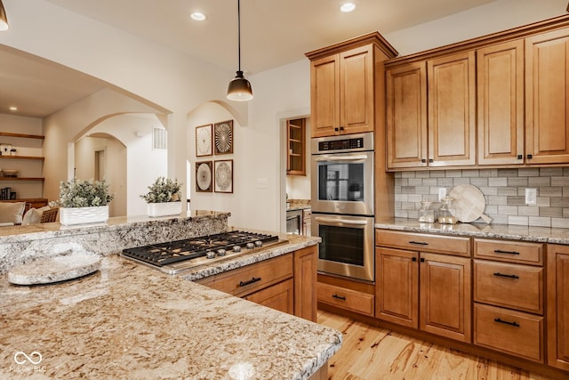 kitchen featuring brown cabinetry, light stone countertops, stainless steel appliances, light wood-style floors, and backsplash