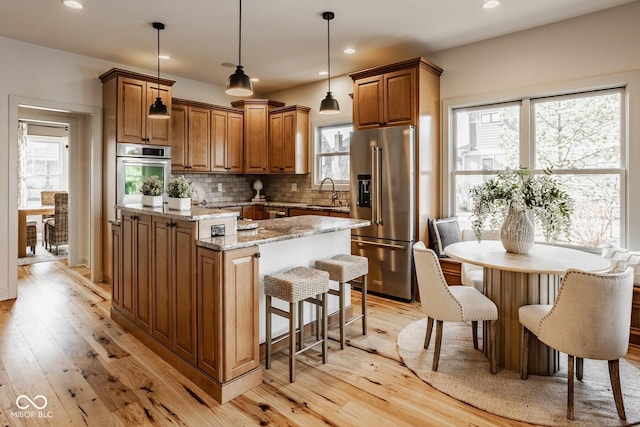 kitchen with a kitchen island, light wood-style flooring, a sink, appliances with stainless steel finishes, and brown cabinets