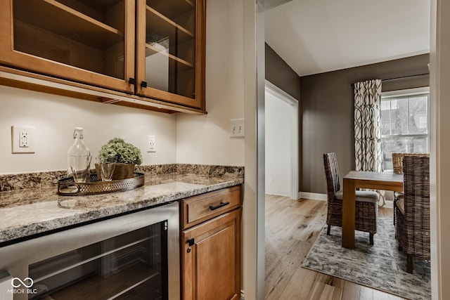 kitchen with brown cabinets, light wood-style flooring, beverage cooler, glass insert cabinets, and baseboards