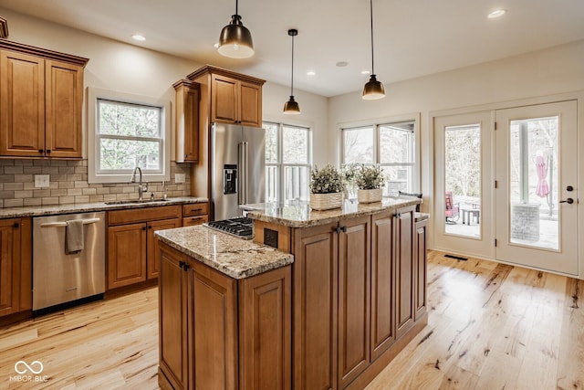 kitchen with a sink, decorative backsplash, appliances with stainless steel finishes, brown cabinets, and a center island