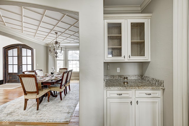 dining space featuring arched walkways, light wood-style flooring, french doors, and crown molding