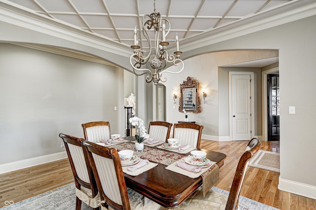 dining space featuring baseboards, light wood finished floors, coffered ceiling, an inviting chandelier, and arched walkways