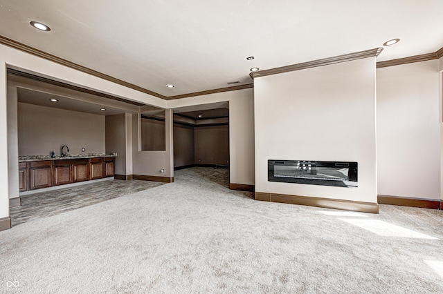 unfurnished living room with a glass covered fireplace, ornamental molding, carpet flooring, and a sink