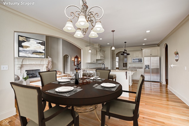 dining room featuring light wood-style flooring, recessed lighting, arched walkways, a fireplace, and crown molding