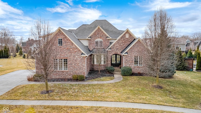 traditional-style home featuring driveway, brick siding, roof with shingles, and a front yard