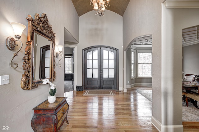 entrance foyer featuring baseboards, arched walkways, vaulted ceiling, french doors, and wood-type flooring