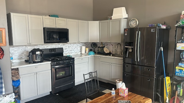 kitchen featuring black appliances, a sink, backsplash, white cabinetry, and light countertops