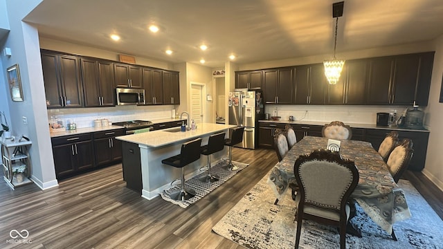 kitchen with an island with sink, a sink, dark wood finished floors, stainless steel appliances, and a breakfast bar area