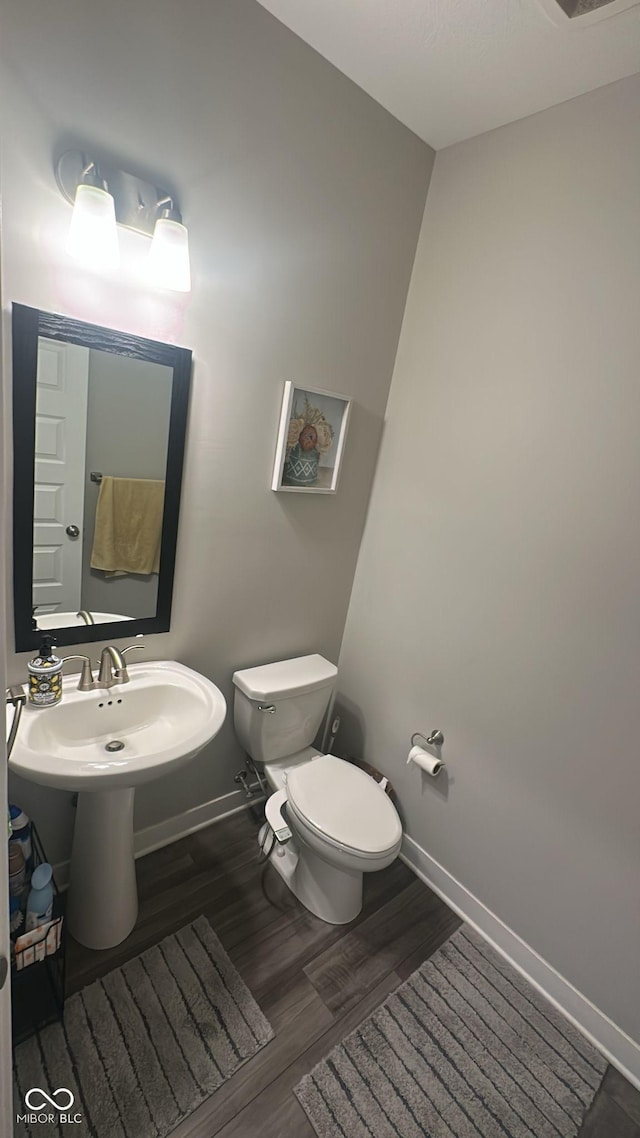 bathroom featuring toilet, wood finished floors, baseboards, and a sink