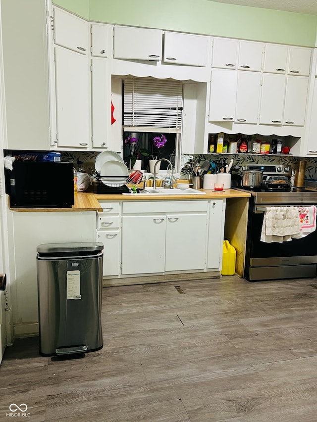 kitchen featuring black microwave, electric stove, light wood-style floors, white cabinets, and a sink