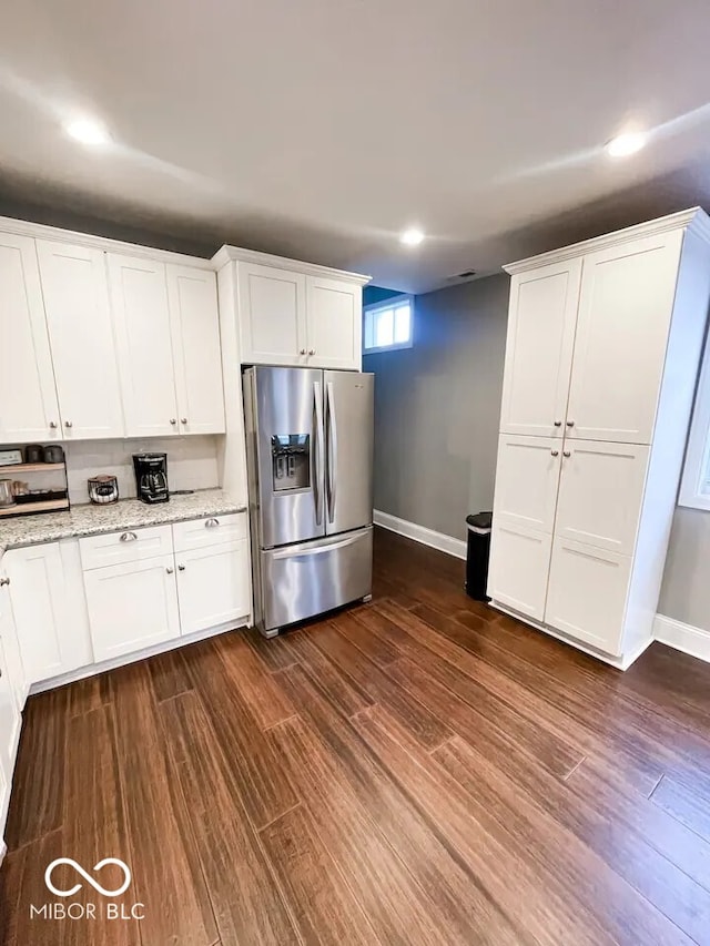 kitchen with stainless steel fridge, light stone counters, white cabinets, and dark wood-type flooring