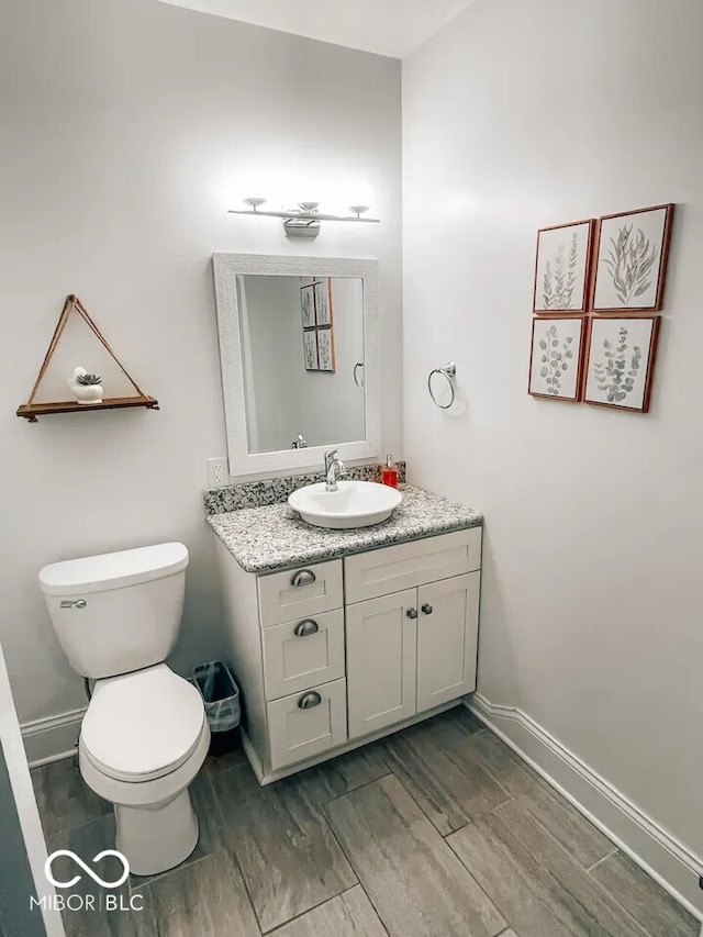 bathroom featuring toilet, baseboards, wood finished floors, and vanity