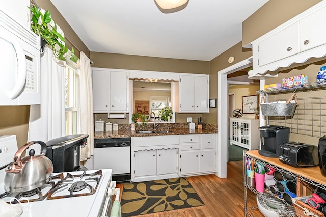 kitchen with dark wood-type flooring, dark stone counters, white appliances, white cabinetry, and a sink