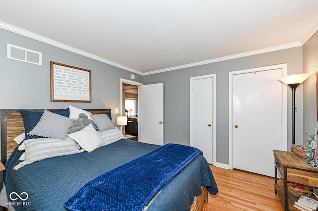 bedroom with light wood finished floors, visible vents, multiple closets, and ornamental molding