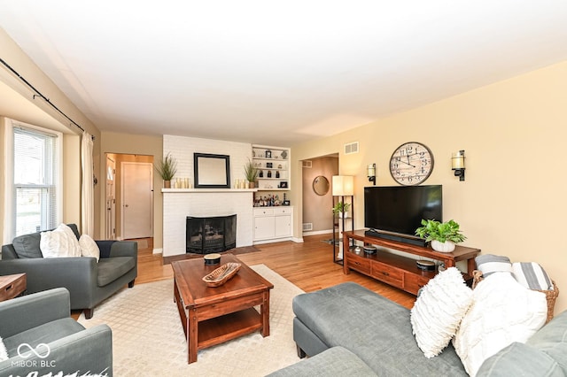 living room featuring visible vents, baseboards, a brick fireplace, and wood finished floors