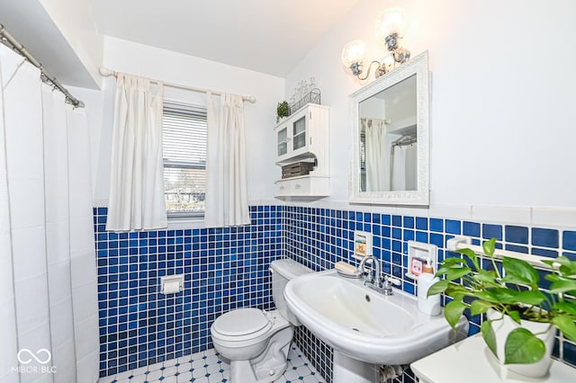 bathroom featuring tile patterned flooring, toilet, wainscoting, tile walls, and a sink