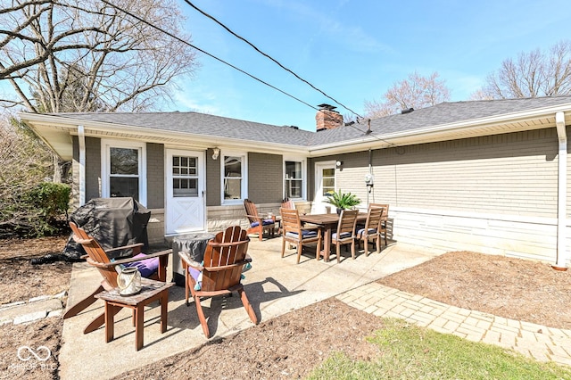 rear view of property featuring a patio, brick siding, roof with shingles, and a chimney