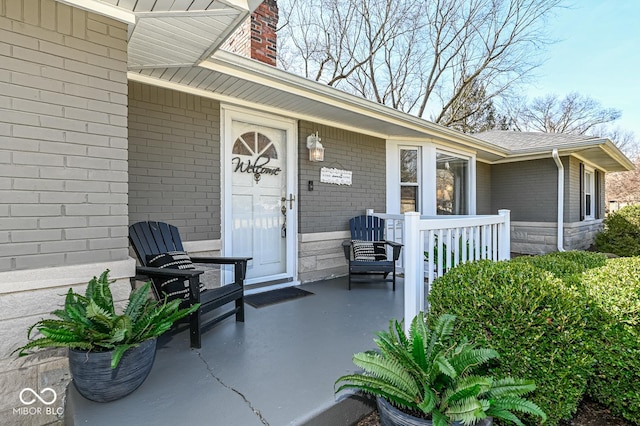 entrance to property featuring covered porch, brick siding, and a chimney