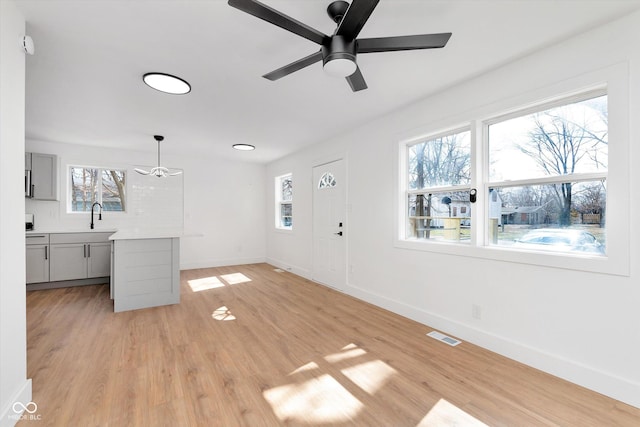 unfurnished living room featuring ceiling fan, light wood-style flooring, a sink, visible vents, and baseboards