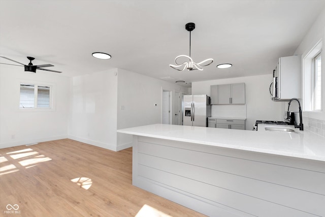 kitchen with stainless steel appliances, a peninsula, a sink, light wood-type flooring, and gray cabinets