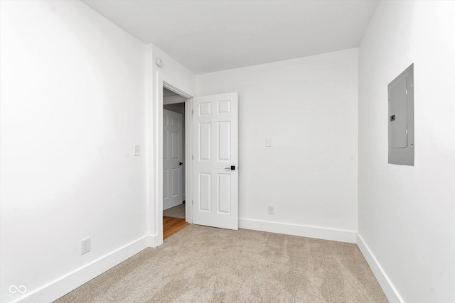 empty room featuring electric panel, light carpet, and baseboards