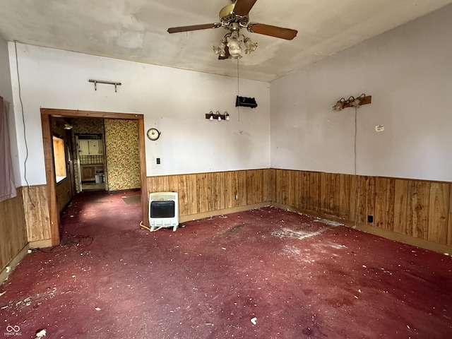 carpeted empty room with wooden walls, heating unit, a ceiling fan, and wainscoting