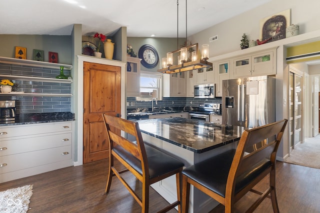 kitchen featuring tasteful backsplash, glass insert cabinets, a kitchen bar, vaulted ceiling, and appliances with stainless steel finishes