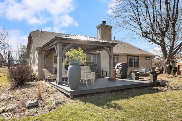 rear view of property with roof with shingles, a chimney, a gazebo, a deck, and a lawn