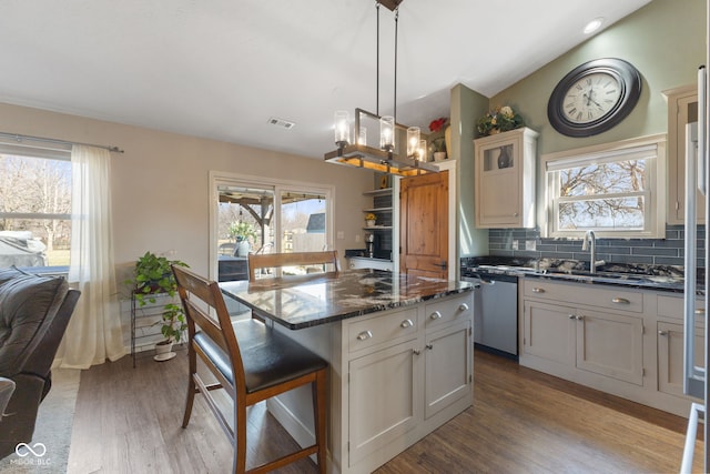 kitchen featuring wood finished floors, lofted ceiling, dishwasher, a kitchen breakfast bar, and tasteful backsplash