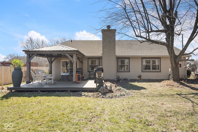 back of house featuring fence, a wooden deck, a chimney, a gazebo, and a lawn