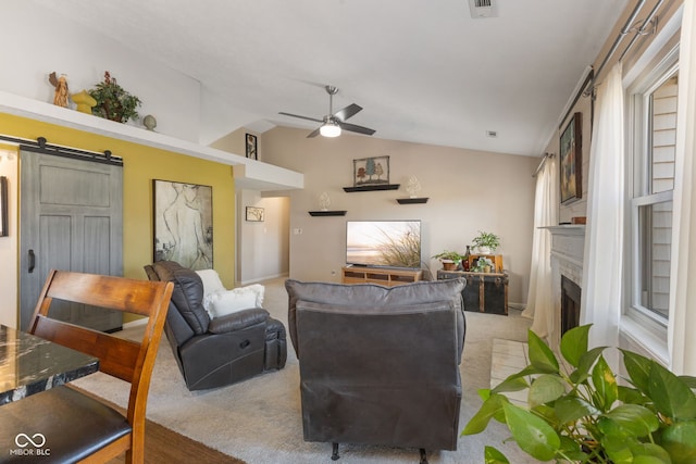 living area with light colored carpet, lofted ceiling, a barn door, a fireplace, and a ceiling fan