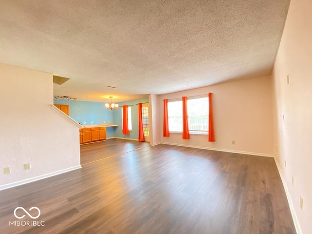 empty room with baseboards, a textured ceiling, a chandelier, and dark wood-type flooring