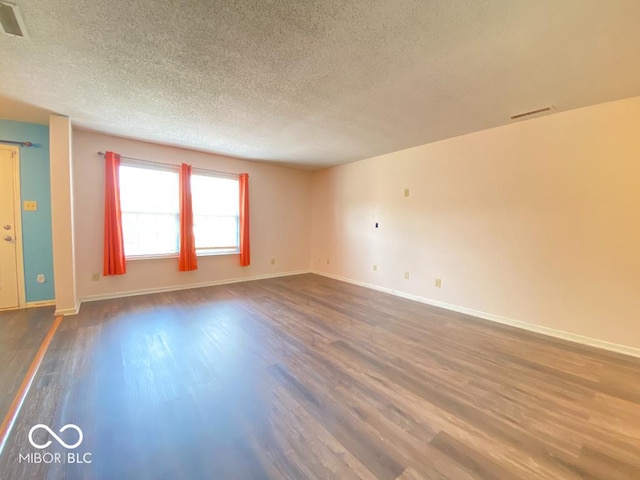 empty room with a textured ceiling, wood finished floors, visible vents, and baseboards