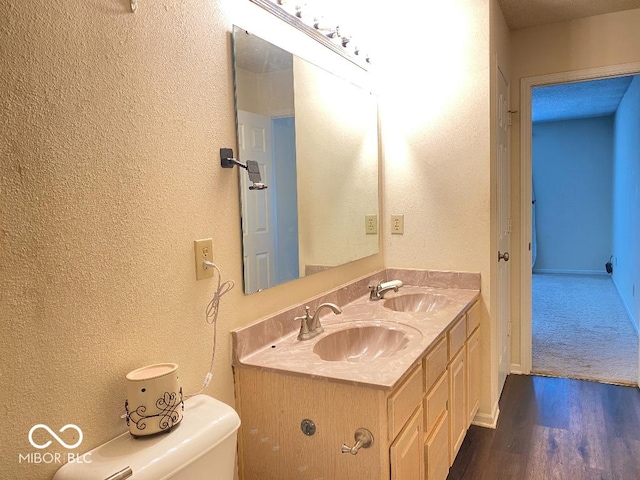 bathroom with double vanity, wood finished floors, a sink, and toilet