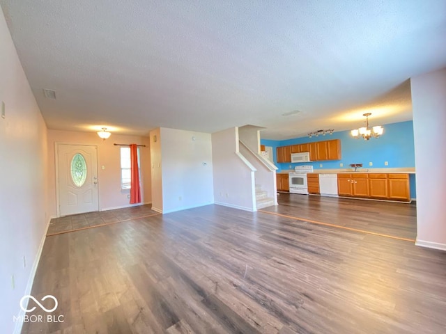 unfurnished living room with stairway, dark wood-style flooring, a notable chandelier, and a textured ceiling