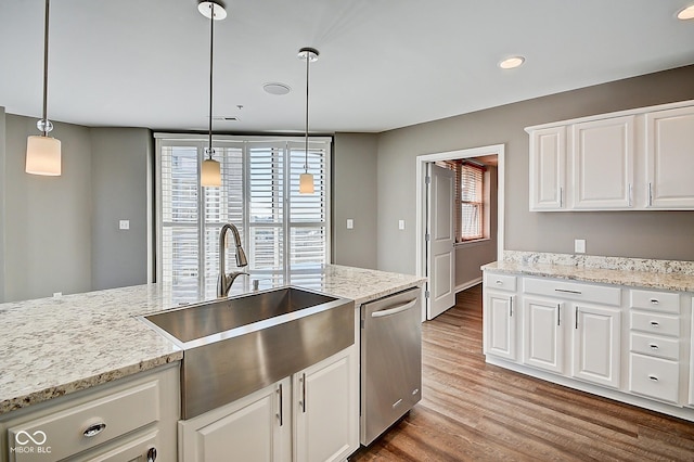 kitchen with light stone countertops, dishwasher, wood finished floors, and a sink