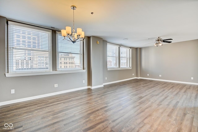 empty room featuring ceiling fan with notable chandelier, wood finished floors, and baseboards