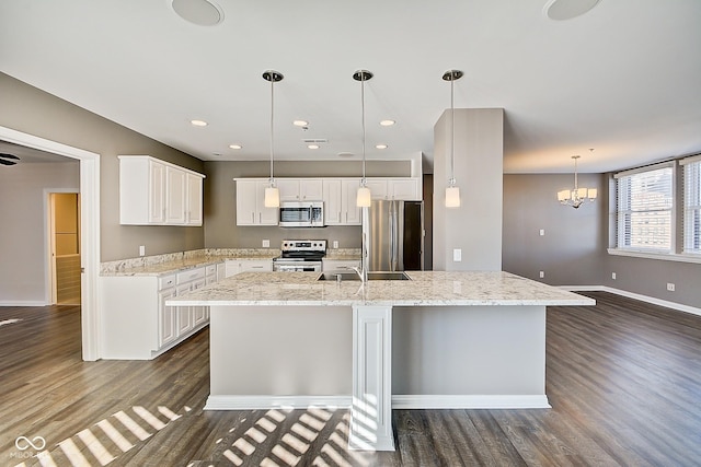 kitchen with dark wood-type flooring, baseboards, appliances with stainless steel finishes, white cabinets, and a kitchen island with sink